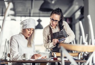 Female chef and waitress with iPad and calculator. Photo.